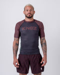 Kingz Noise V2 Rashguard Dark Gray Red - Full Body Front View Male Athlete Short Sleeve Dark Charcoal Body Red Rust Noise Static Dot Pattern Sleeves KINGZ Red Noise Text Matching Noise Pattern Shorts Crown Logo BJJ No-Gi Training
