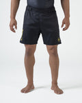 Kingz MI-K Roots Onça Pintada Shorts Black - Full Body Front View Male Athlete Dark Charcoal Black KINGZ Gold Vertical Text Left Leg MI-K Circular Crown Badge Right Thigh Subtle Texture Competition Cut Men's Grappling Shorts No-Gi BJJ MI-K Roots Jaguar Collection [color:Black]