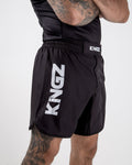 Kingz Kore Shorts V1 Black - Side View Tattooed Male Athlete Bold KINGZ Vertical Logo Left Thigh Elastic Waistband Modern Cut Durable Fabric Men's Grappling Shorts No-Gi BJJ